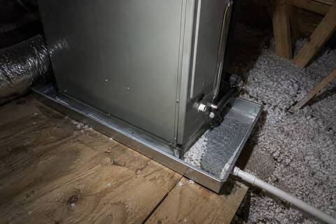 Air handler standing in a metal pan in an attic, insulation and framing around it