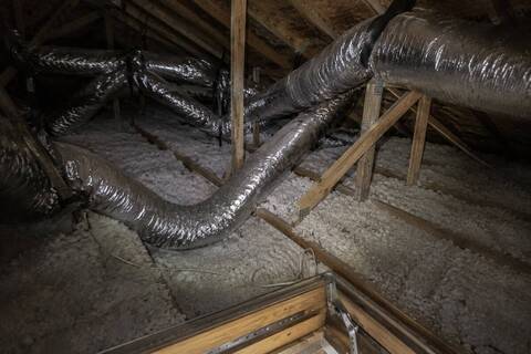 Flexible duct runs crossing an attic above blown-in insulation, one section sagging between joists