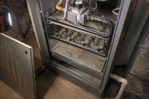 Open burner compartment on a furnace with dust and debris across the burner tray