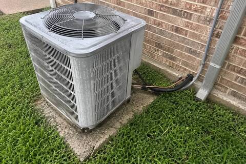 Weathered outdoor condenser unit sitting on a cracked concrete pad beside a brick wall
