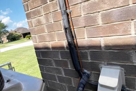 Refrigerant lines running up a brick exterior wall with taped insulation at one joint
