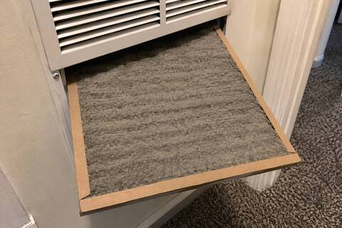 Pleated filter pulled part way out of a return grille, gray dust across the face of it