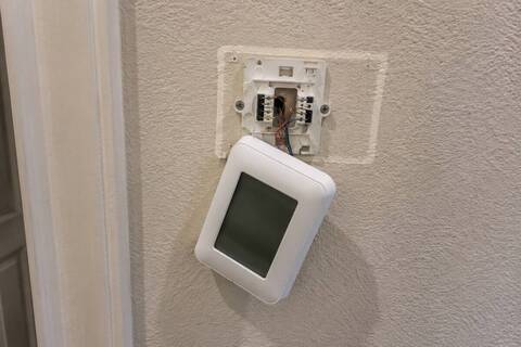 Wall thermostat beside an open base plate with the low-voltage wiring exposed