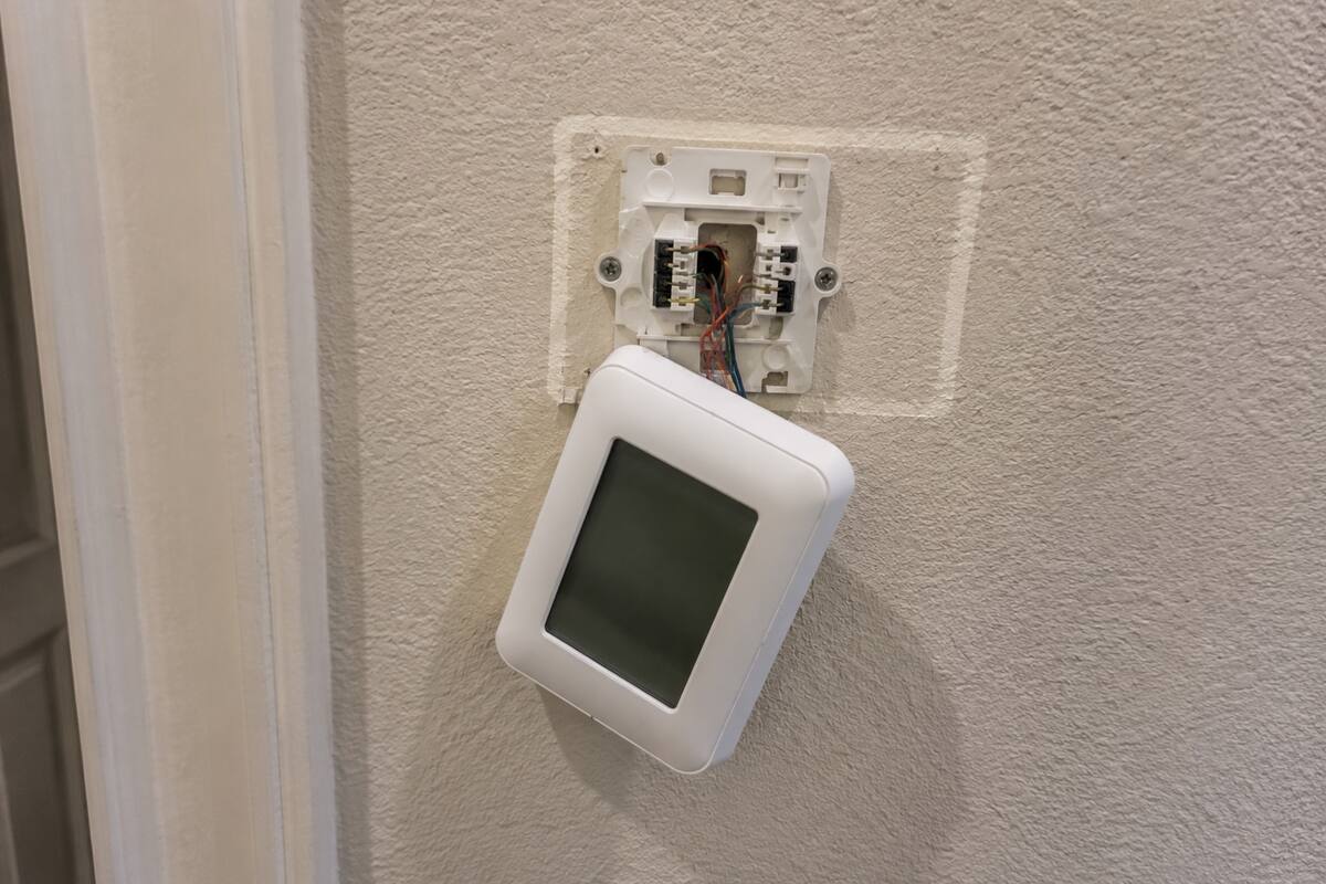 Wall thermostat beside an open base plate with the low-voltage wiring exposed